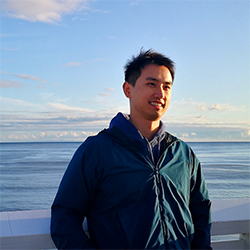 Image of Lei Shi who is an Asian man with black hair standing by the sea, wearing a green hoodie
