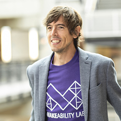 Jon Froehlich is a white man with brown hair wearing a purple 'Makeability Lab' t-shirt and a gray sports coat